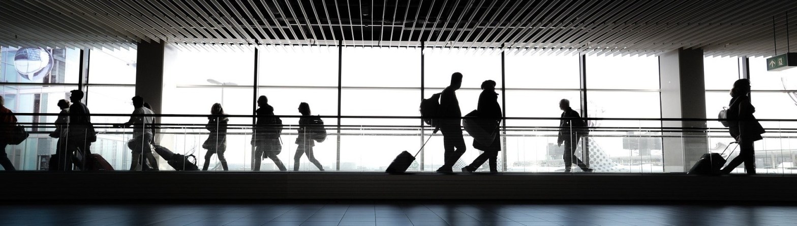 La imagen muestra en primer plano personas deambulando en un aeropuerto con total normalidad. Al fondo una pared acristalada en la que se pueden intuir algunos aviones a lo lejos.
