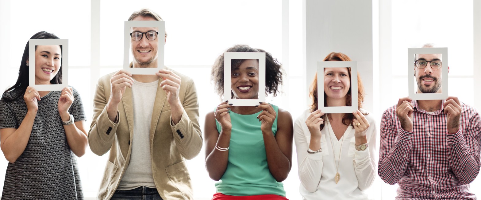 La imagen muestra un grupo de cinco personas con diversidad de género, tono de piel, color y tipo de cabello, etc. Cada persona sujeta un marco blanco justo delante de su cara.
