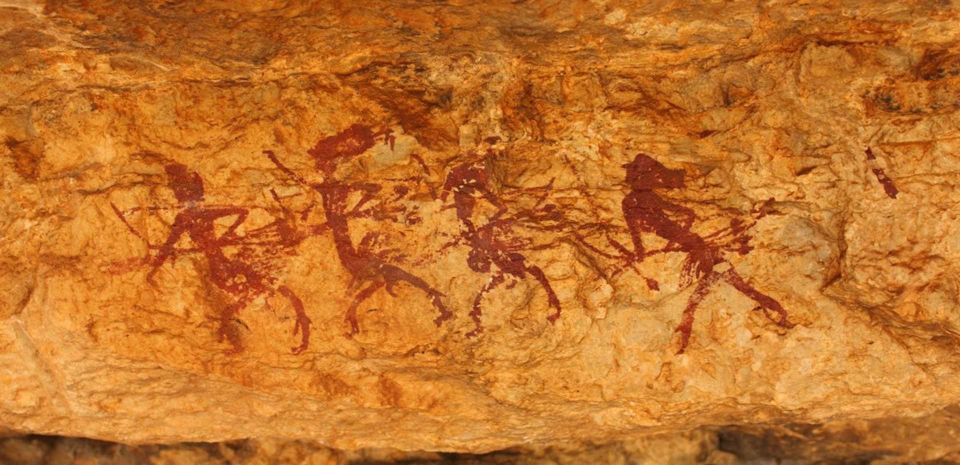 La imagen muestra una escena de arte rupestre levantino sobre roca, formada por 4 figuras humanas que tienen el mismo tamaño y parecer mirar hacia la misma dirección, con las piernas abiertas y objetos y ornamentas en brazos, cabeza y cuerpo.
Esta escena de danza fue localizada en Abrigo de Voro.