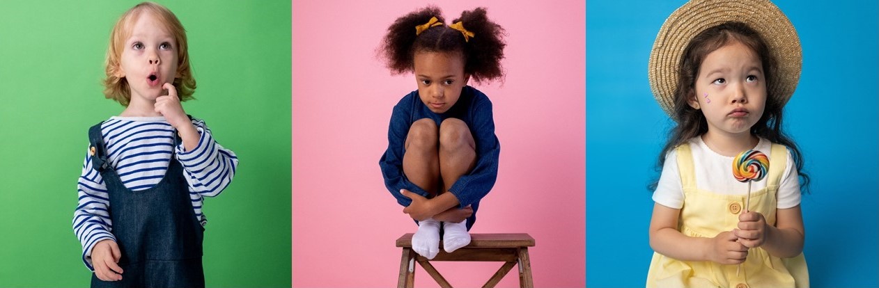 La imagen esta dividida en tres partes y en cada una de ellas vemos una niña con una expresión de emociones diferente. A la izquierda una niña rubia con un peto y una camiseta a rayas tiene un rostro de sorpresa. En el centro una niña de tez oscura con dos colitas sujetas con lazos está sentada encima de un taburete cogiéndose ambas piernas en un signo de tristeza. A la derecha vemos una niña con rasgos asiáticos con un vestido amarillo y un sombrero de paja, sujetando una piruleta de colores y mirando hacia arriba con una mueca de enfado.