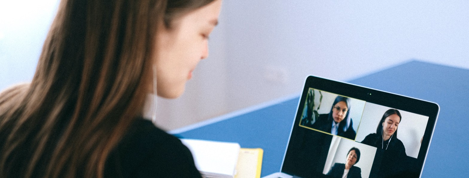 La imagen muestra una mujer desenfocada conectada por videoconferencia a un ordenador portátil con otras dos mujeres, todas ellas vestidas de manera formal.